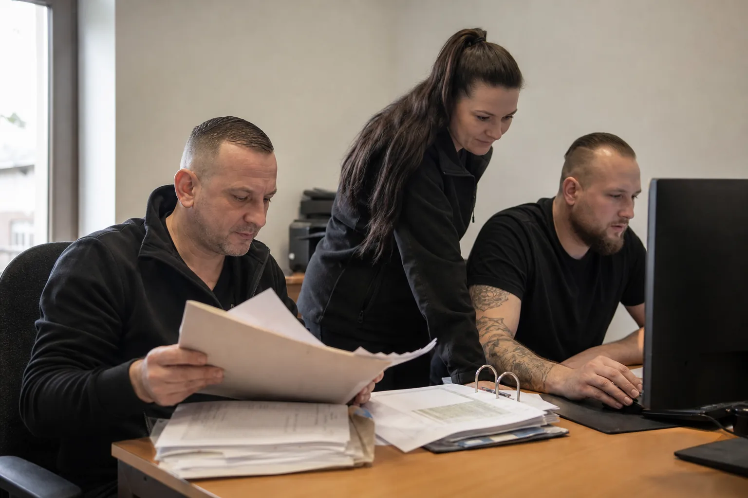 Papierunterlagen, eine Tabellenansicht und eine digitale Akte auf einem Arbeitsplatz